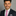 Man wearing a dark suit with a thin pink tie with light blue dots and a silver square against a gray background