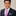 Man wearing a navy suit with a pink tie featuring blue polka dots with a silver square on a neutral background