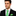 Man wearing a black suit with a green  with blue dots tie and pocket square on a white background