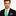 Man wearing a black suit with a green with blue dots tie and blue pocket square on a white background