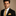 Man wearing a black suit with a yellow thin tie and pocket square on a beige background