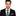 Man wearing a black suit with a blue and gray checkered tie and pocket square on a white background