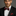 Man wearing a black suit with a red patterned bow tie and pocket square on a gray background