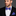 Man wearing a black suit with a purple paisley bow tie and pocket square on a gray background