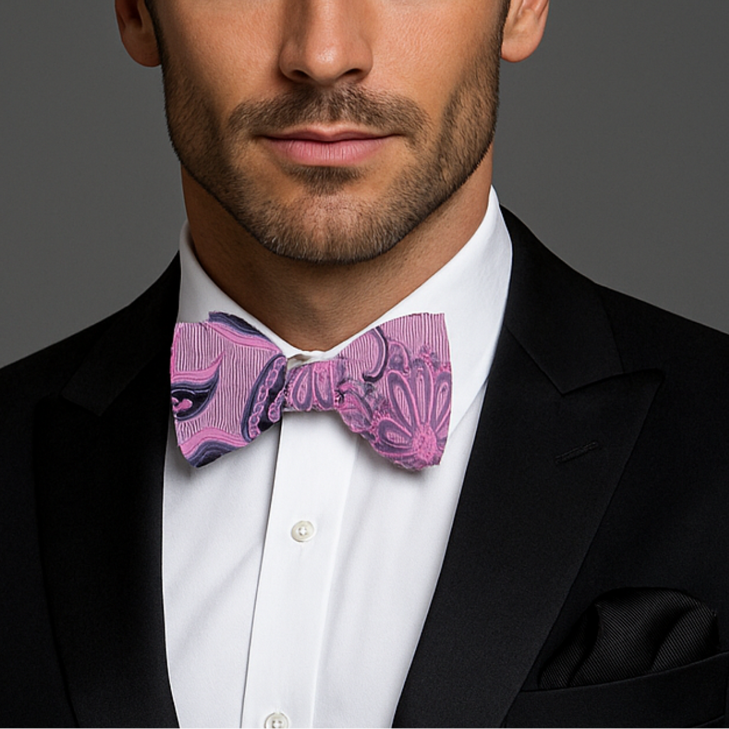 Man wearing a black suit with a white shirt and pink bow tie against a gray background