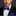 Man wearing a black suit with a blue polka dot bow tie and pocket square on a dark background