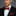 Man wearing a black suit with a red and blue polka bow tie and matching pocket square on a gray background