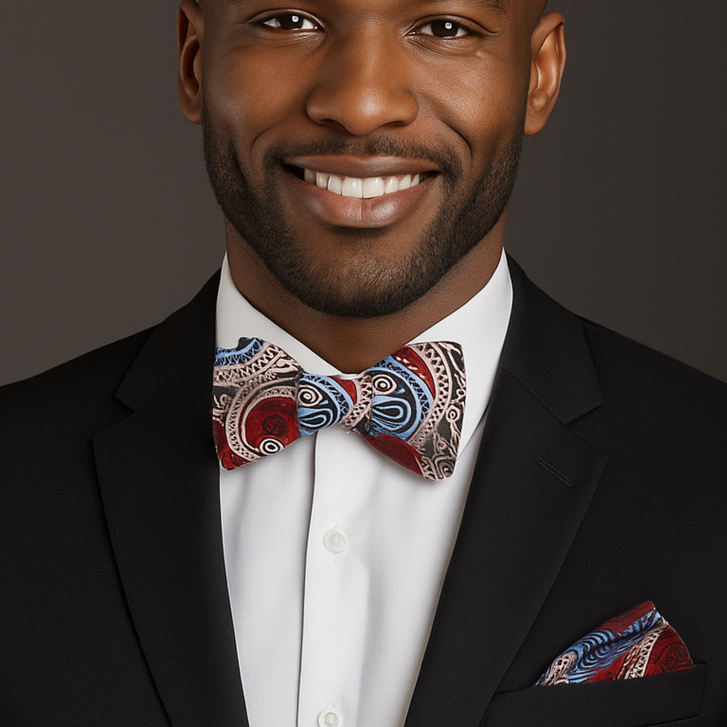 Man wearing a black suit with a colorful bow tie and pocket square on a dark background