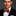 Man wearing a black suit with a red, yellow and dark blue striped bow tie on a dark background
