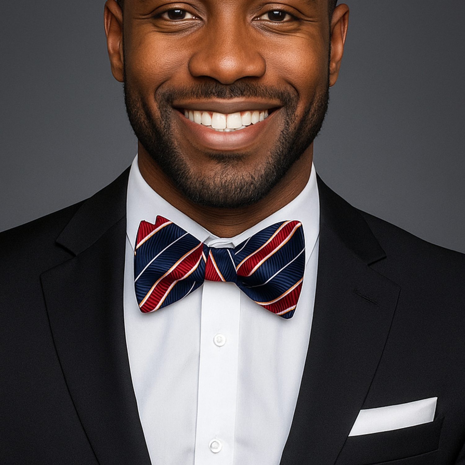 Man wearing a black suit with a red, white, and blue striped bow tie against a gray background