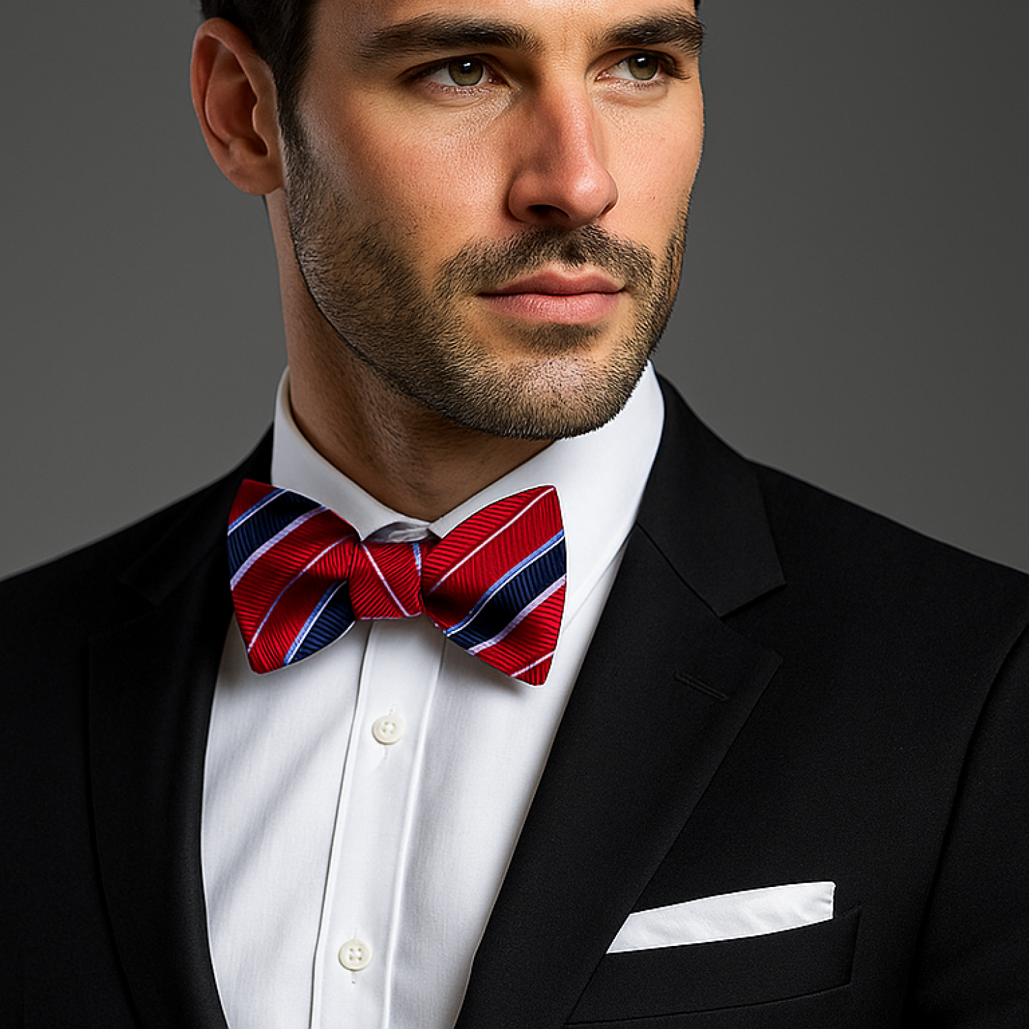 Man wearing a black suit with a red and blue striped bow tie on a gray background