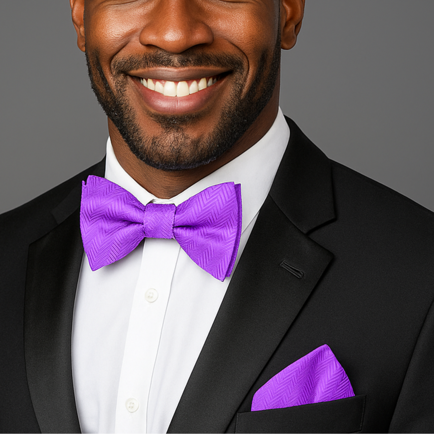 Man wearing a black suit with a purple bow tie and pocket square on a gray background