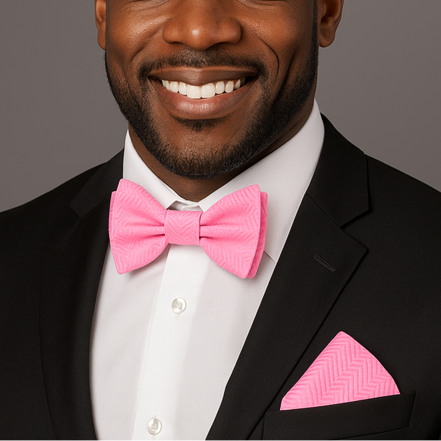 Man wearing a black suit with a pink bow tie and pocket square on a gray background