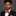 Man wearing a black suit with an orange and red patterned bow tie and pocket square on a gray background