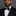 Man wearing a black suit with a white shirt and black with red dots patterned bow tie on a gray background