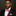 Man wearing a black suit with a red geometric bow tie and pocket square on a dark background