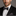 Man wearing a black suit with a white shirt and purple bow tie against a gray background