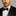 Man wearing a black tuxedo with a black bow tie against a gray background