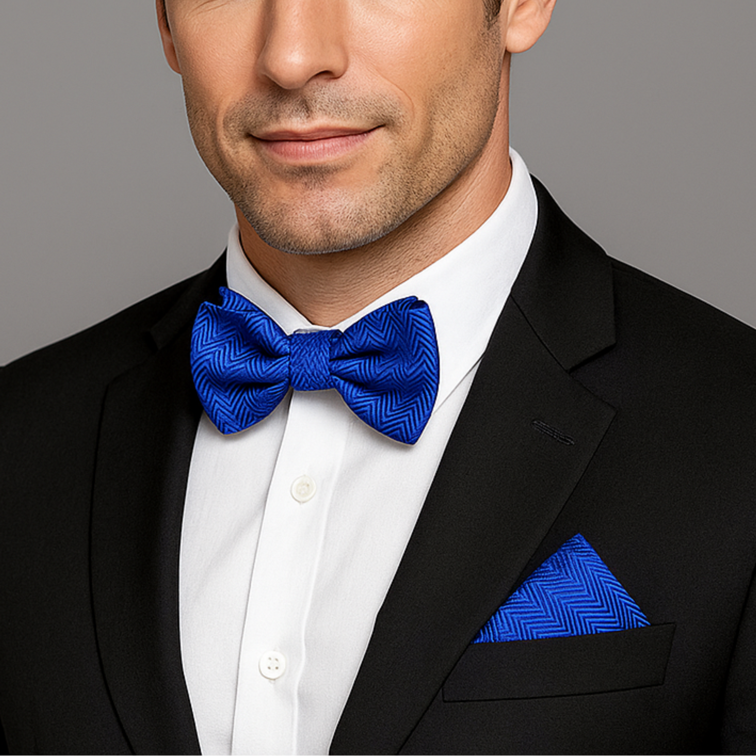 Man wearing a black suit with a blue bow tie and pocket square on a gray background