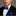 Man wearing a black suit with a white shirt and blue bow tie and pocket square on a gray background