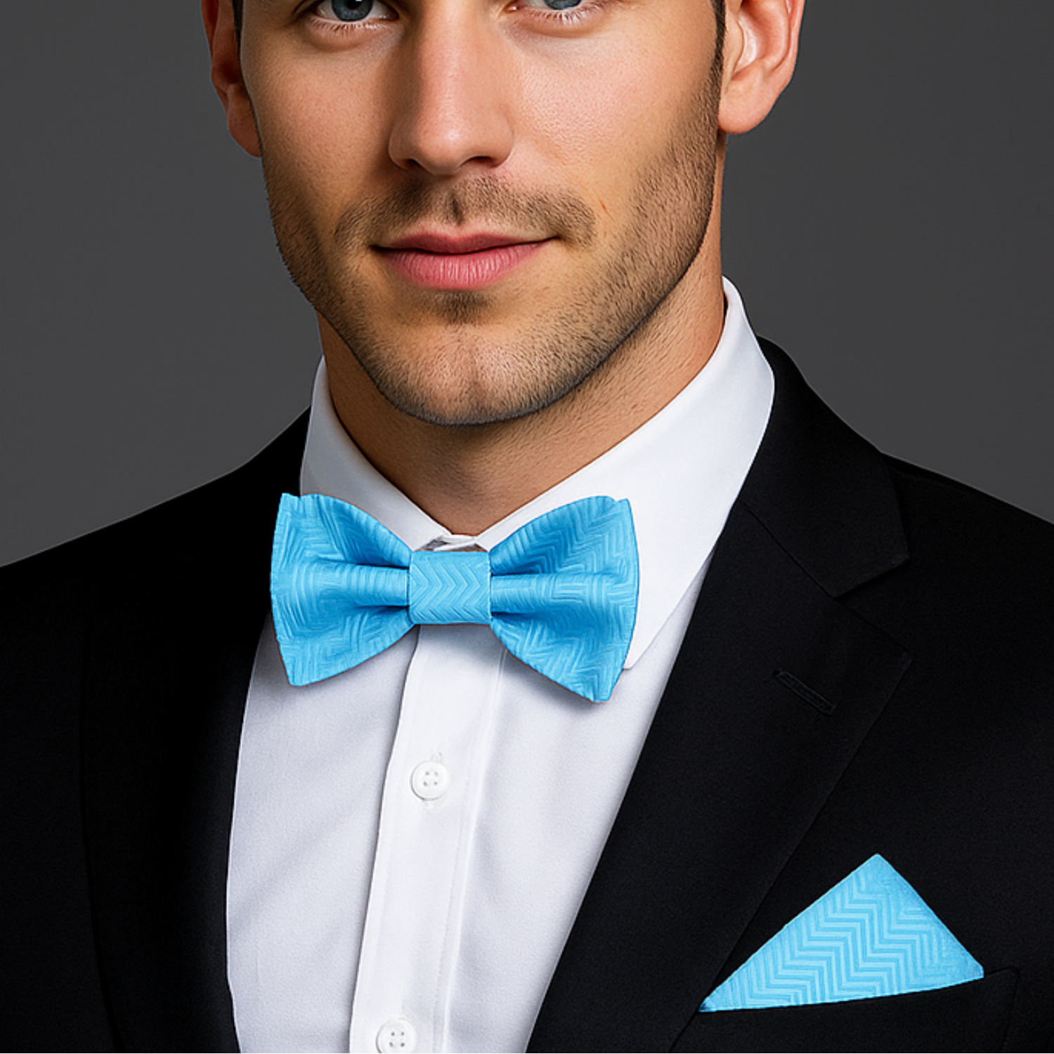 Man wearing a black suit with a electric blue bow tie and pocket square on a gray background