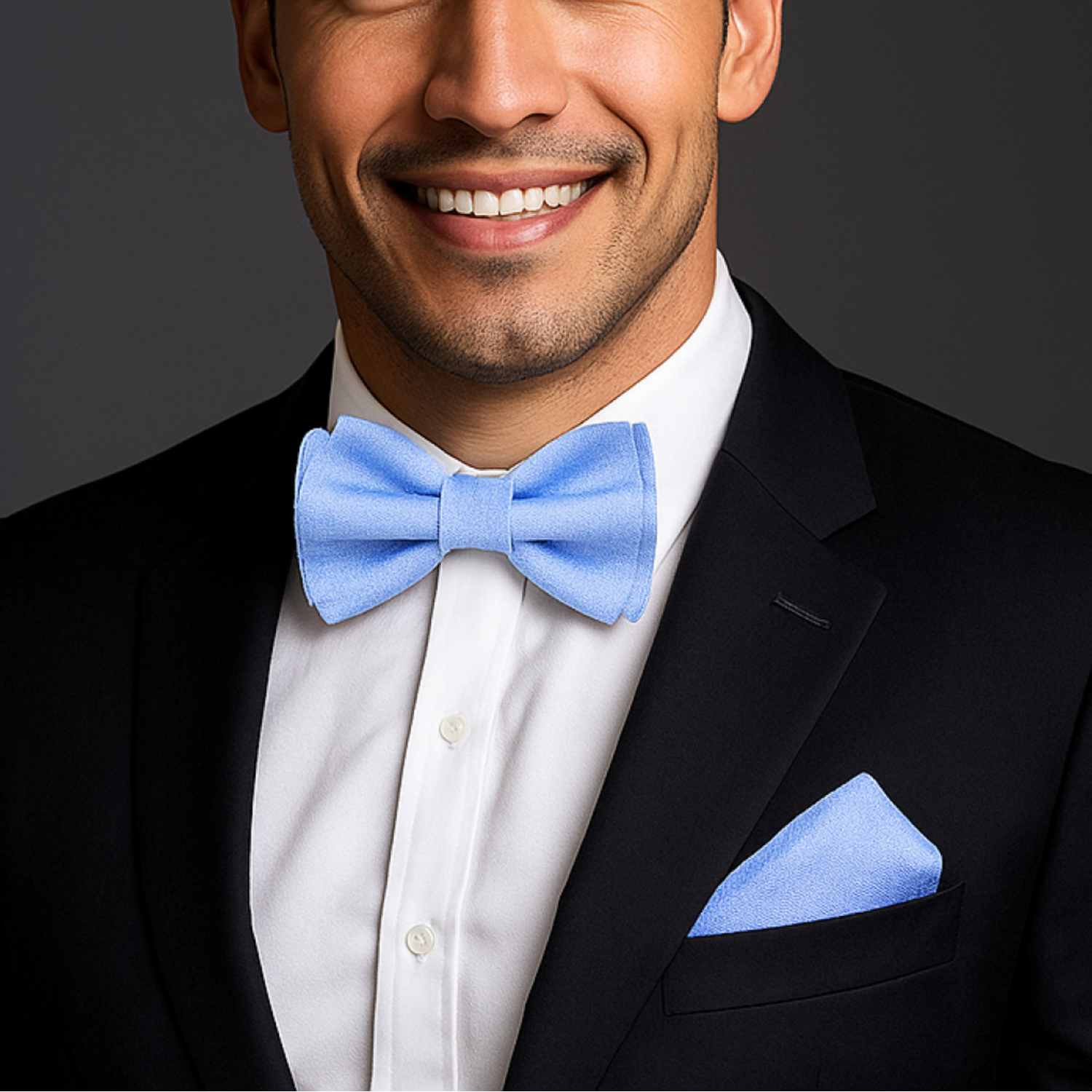 Man wearing a black tuxedo with a blue bow tie and pocket square on a dark background