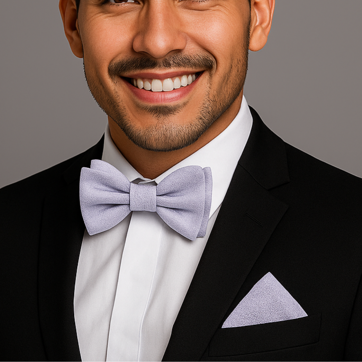 Man wearing a black suit with a white shirt and grey bow tie on a gray background