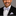 Man wearing a black suit with a white shirt and grey bow tie on a gray background