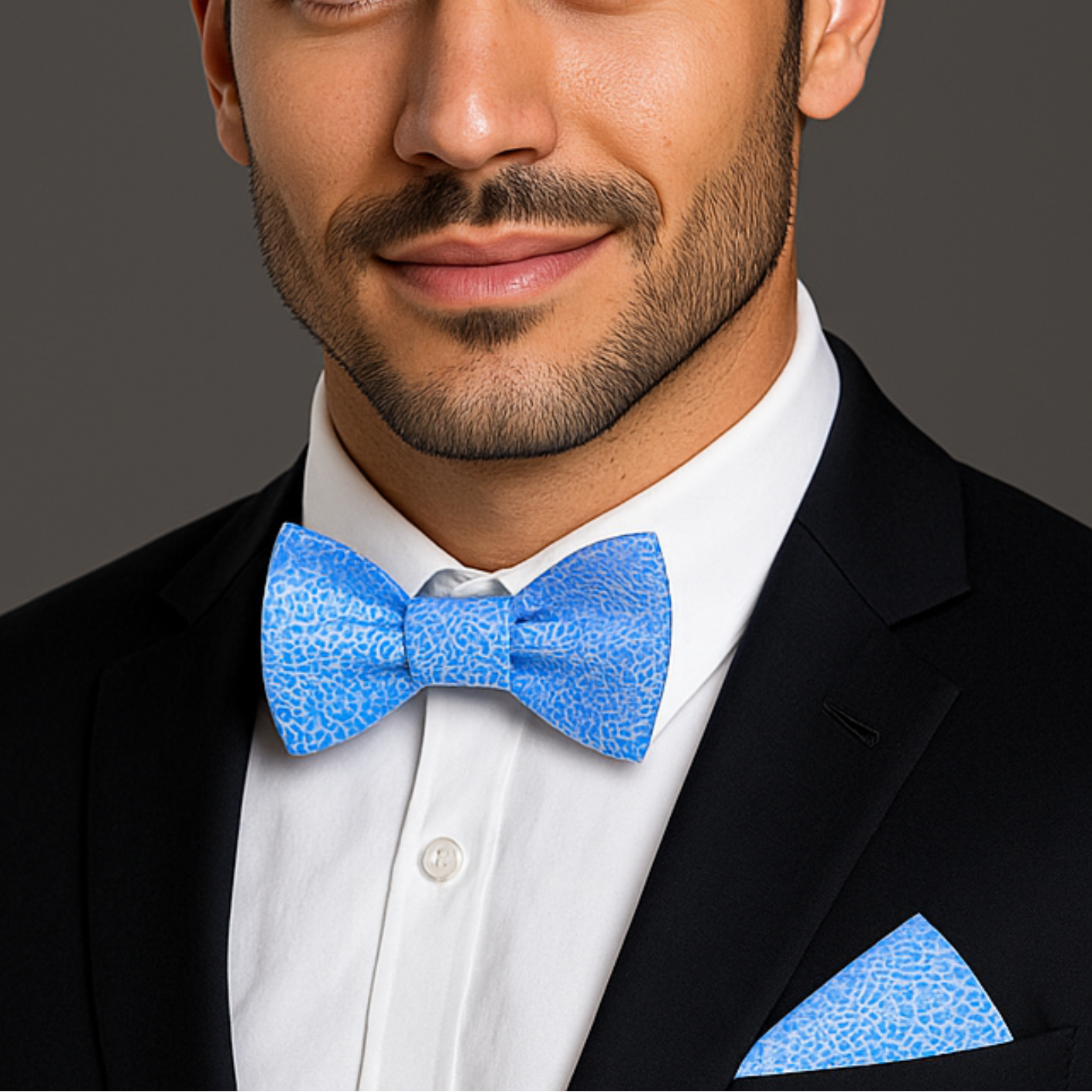 Man wearing a black suit with a blue bow tie and pocket square on a gray background