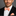Man wearing a black suit with a coral bow tie and pocket square on a gray background