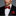 Man wearing a black suit with a Garnet Red Solid Pattern Self Tie Bow Tie, Matching Pocket Square on a gray background