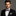 Man wearing a black suit with a colorful red, blue and yellow swirls bow tie and pocket square on a gray background