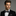 Man wearing a black suit with a olive green and blue geometric bow tie against a gray background
