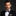Man wearing a black suit with a white shirt and patterned bow tie on a dark background