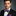 Man wearing a black suit with a colorful pink, blue and yellow paisley bow tie and pocket square on a gray background