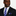 Man wearing a black suit with a blue striped tie and pocket square on a white background