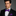 Man wearing a black suit with a purple bow tie and matching pocket square on a gray background