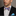 Man wearing a black suit with a colorful purple, blue and gold with a a paisley pattern bow tie and blue handkerchief against a gray background