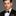 Man wearing a black suit with a blue with brown pinstripe bow tie and pocket square on a gray background