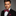 Man wearing a black suit with a deep red with yellow gold squares bow tie and rosewood pocket square on a gray background