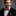 Man wearing a black suit with a red bow tie with brown square against a gray background