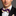 Man wearing a black suit with a purple bow tie featuring yellow stripes on a gray background
