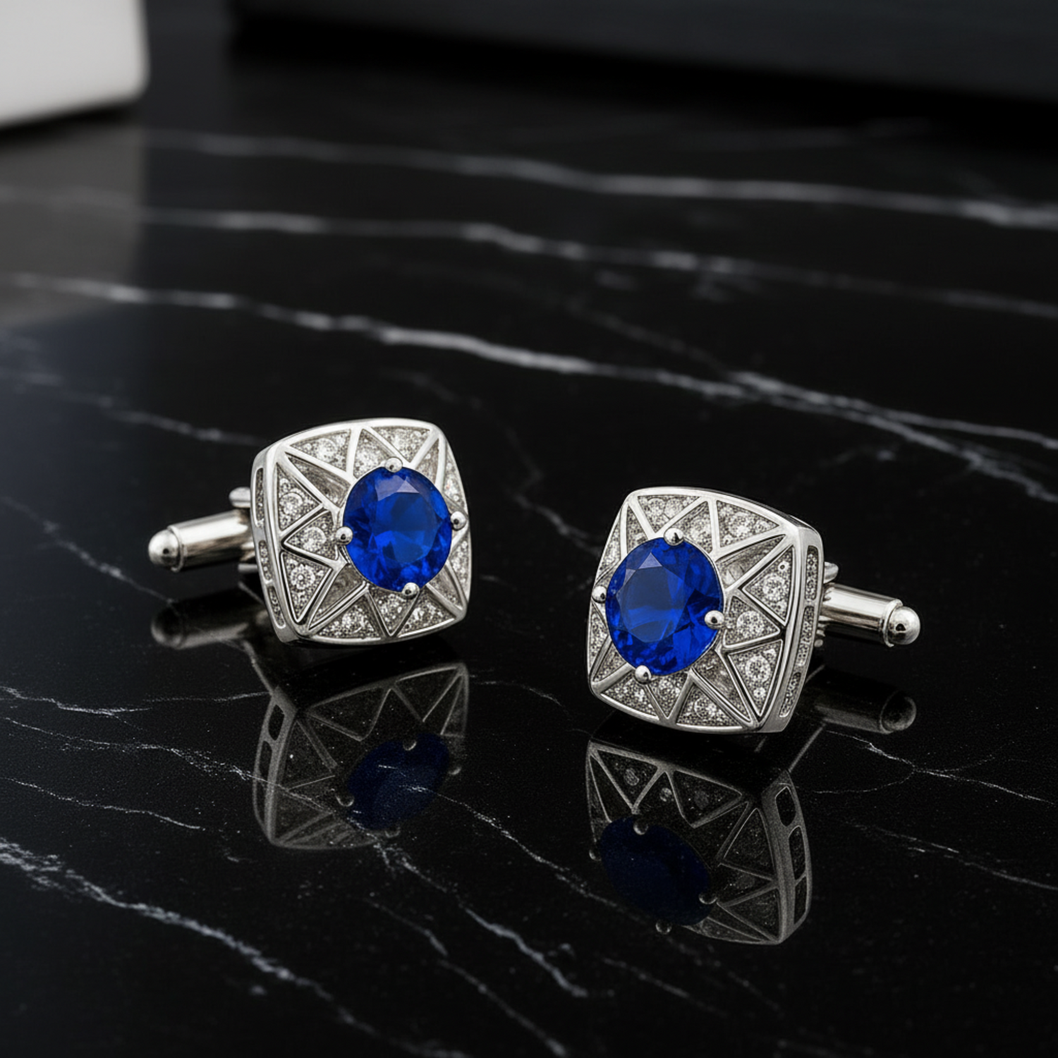 Pair of silver cufflinks with blue gemstones on a black marble surface