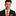 Man wearing a dark suit with an orange tie and pocket square on a gray background