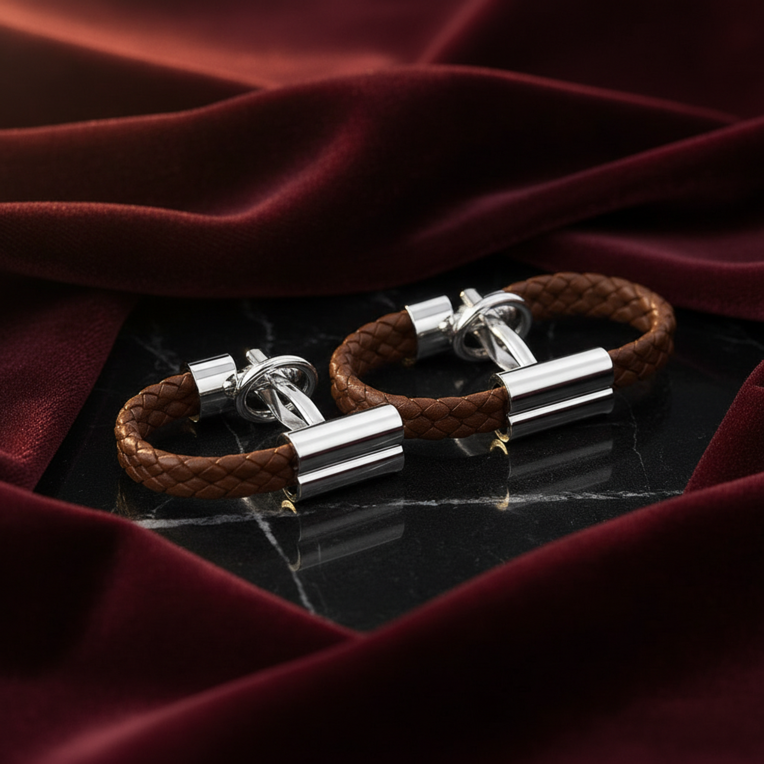 Pair of silver cufflinks with brown braided leather straps on a black marble surface