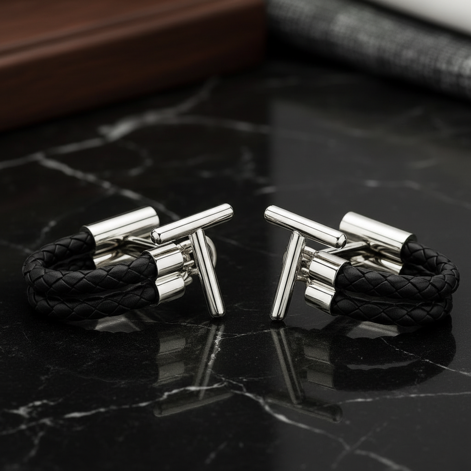 Black braided leather cufflinks with silver clasp on a dark marble surface