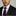 Man wearing a black suit with a purple tie and pocket square on a gray background