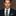 Man wearing a dark suit with a brown and green paisley and stripe patterned tie and pocket square against a neutral background