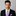 Man wearing a black suit with a white shirt and purple tie and pocket square on a gray background
