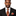 Man wearing a black suit with a patterned tie and pocket square on a white background